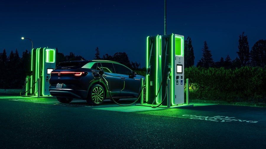 An ID.4 SUV in Tourmaline Blue Metallic is parked at night, charging at a neon lit charging station.